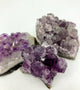 Purple gemstone crystal clusters sit against a white background.